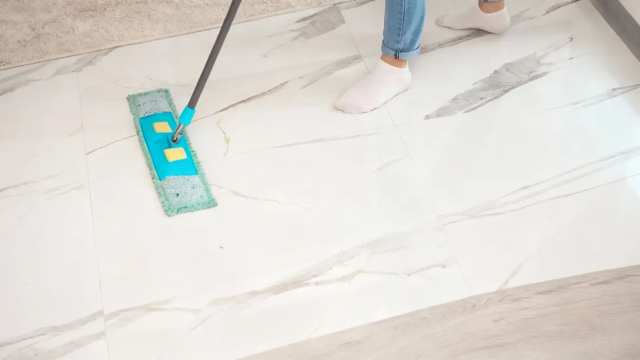 Una persona pulisce un pavimento chiaro con un mocio piatto