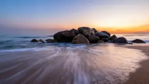 Tramonto sul mare con onde che lambiscono rocce sulla spiaggia