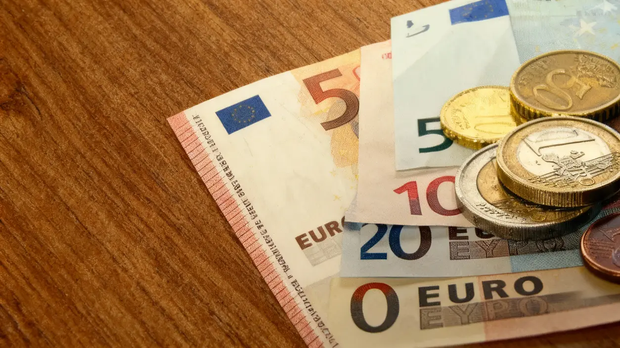Banconote e monete in euro su una superficie di legno