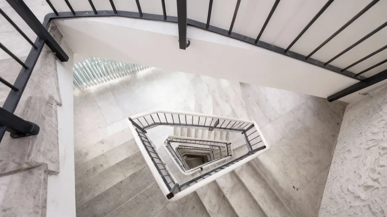 Scala condominiale vista dall'alto con gradini in marmo chiaro e ringhiere metalliche