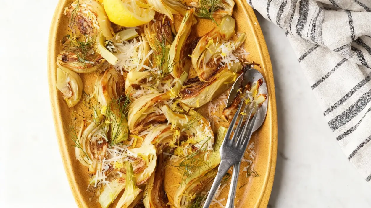 Finocchi al forno dorati serviti su un piatto con scaglie di parmigiano e scorza di limone