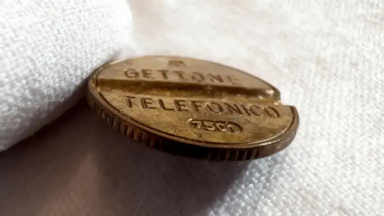Vecchio gettone telefonico italiano appoggiato su un tessuto bianco