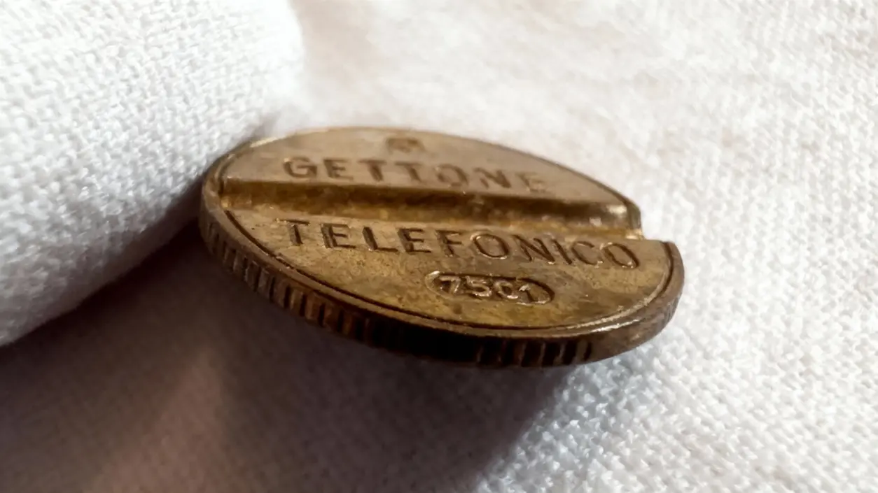Vecchio gettone telefonico italiano appoggiato su un tessuto bianco