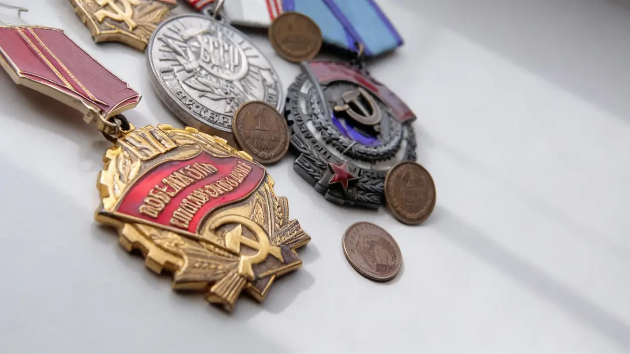 Vecchie medaglie e monete sovietiche disposte su una superficie chiara